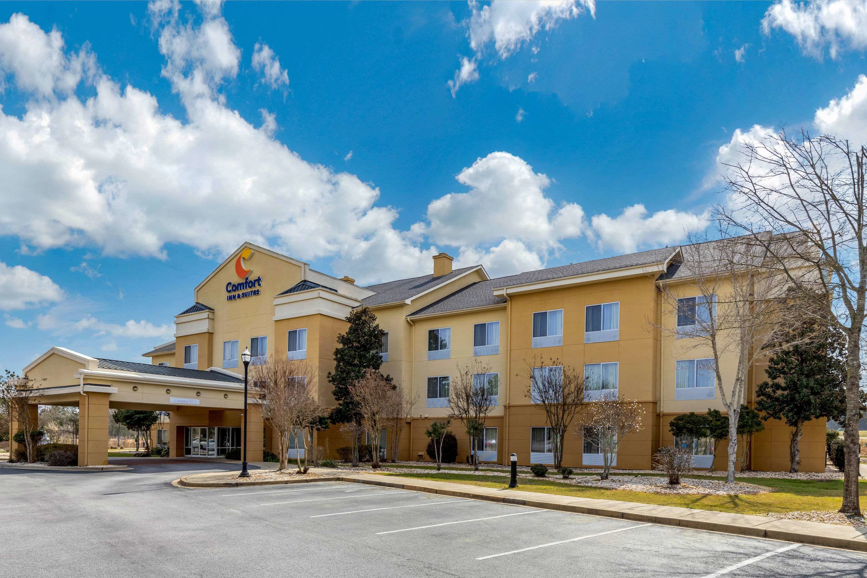 A hotel with a yellow facade, multiple windows, and a parking lot.