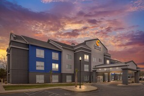 A multi-story hotel with a blue and gray facade, a prominent logo, and a well-lit entrance.
