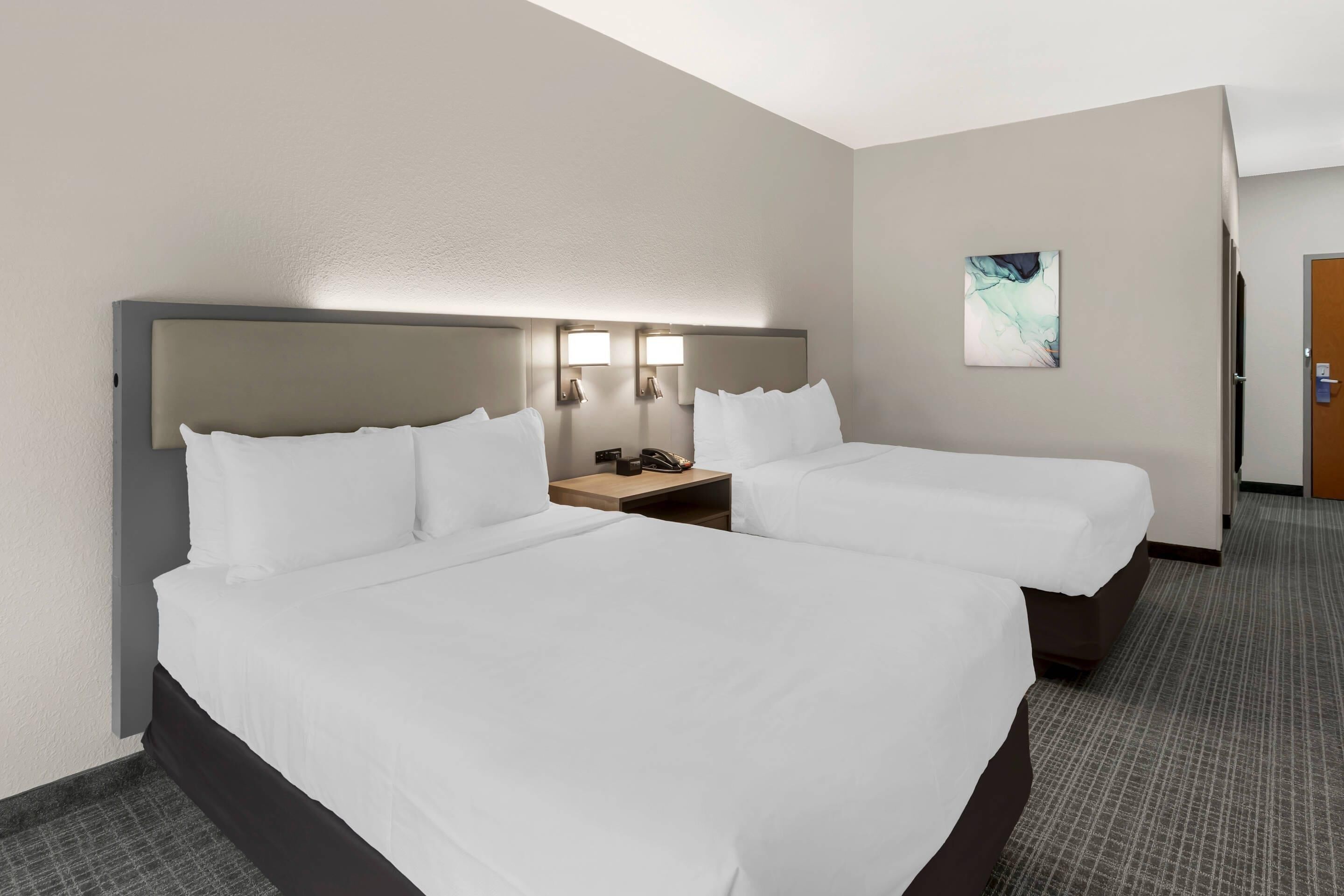Ein Hotelzimmer mit zwei Betten, einem Nachttisch, einer Wandleuchte und einer Tür.
