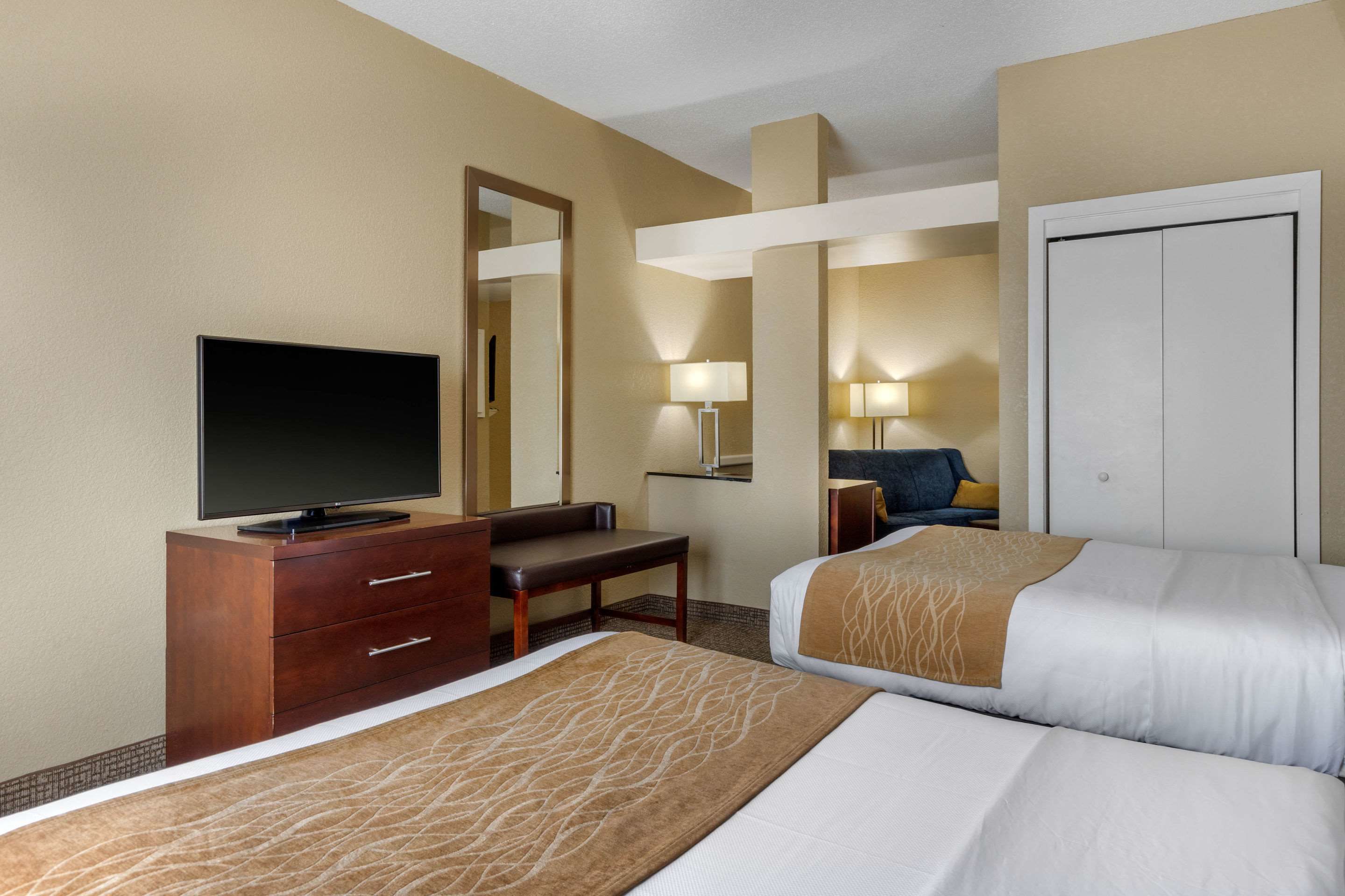 A hotel room with two beds, a TV on a wooden dresser, a desk, and a chair.