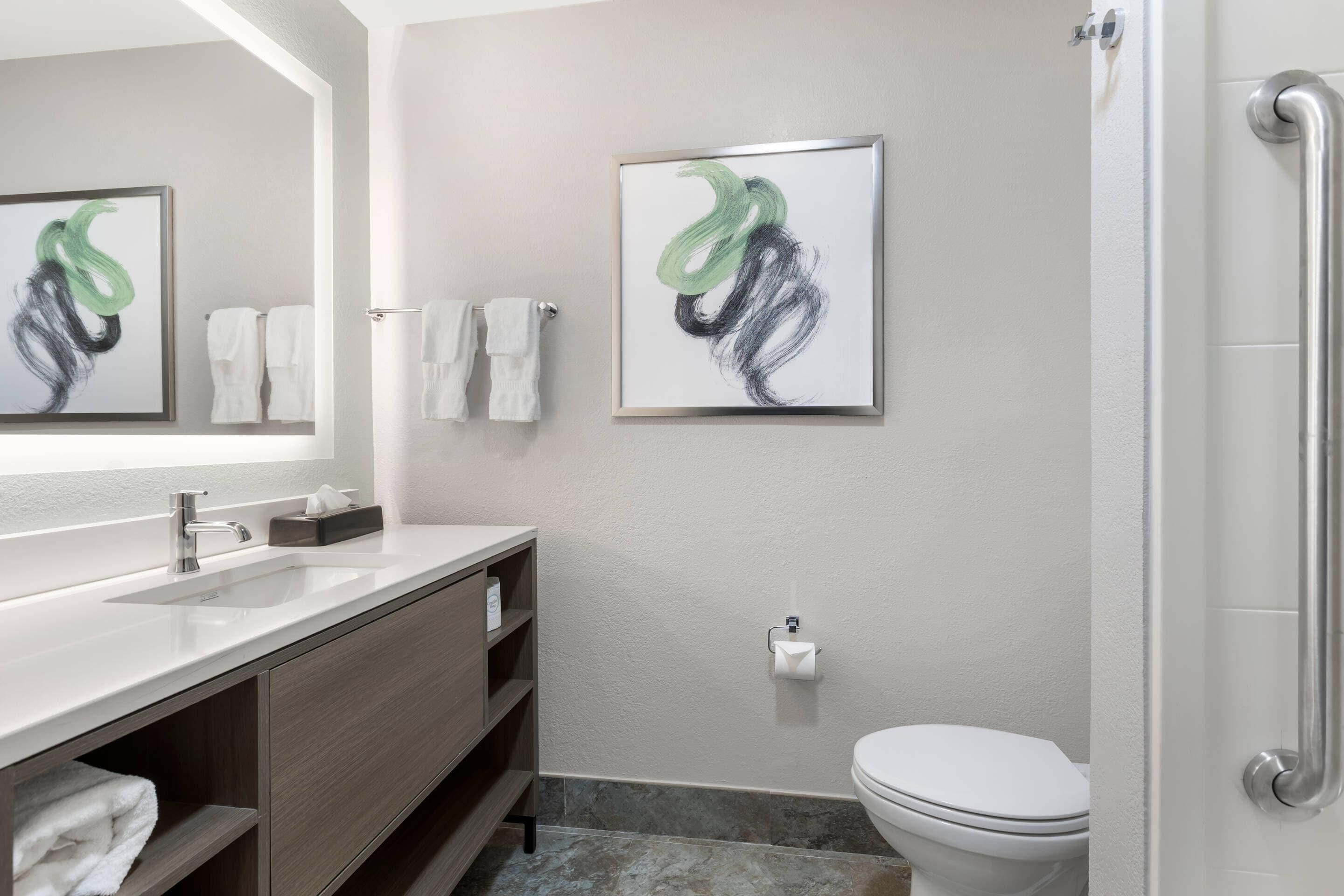 Un baño moderno con lavamanos, espejo, toallero, inodoro y zona de ducha.