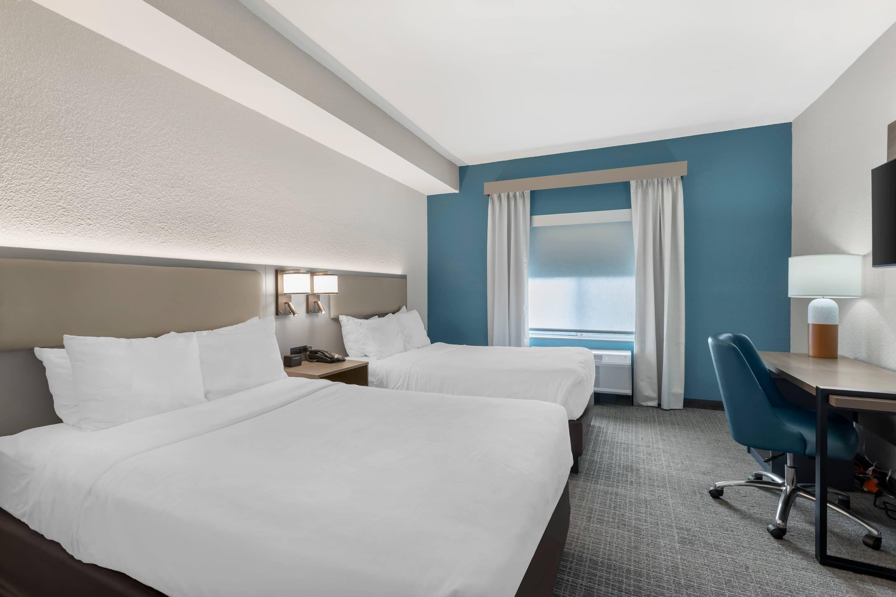 Habitación de hotel con dos camas, un escritorio, una silla, un televisor y una ventana con cortinas.