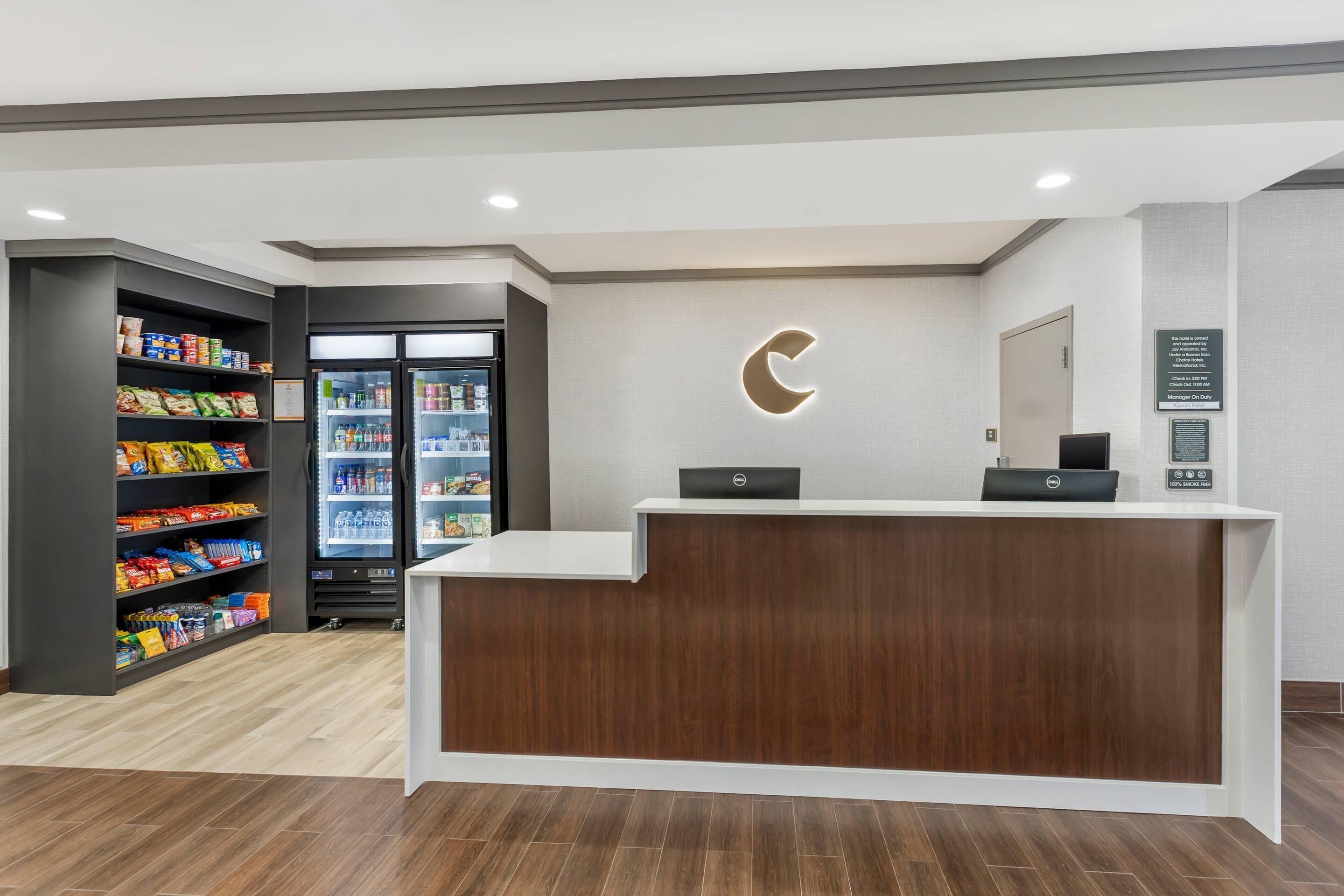 A reception desk with a wooden finish, a refrigerator stocked with beverages, and shelves with snacks.