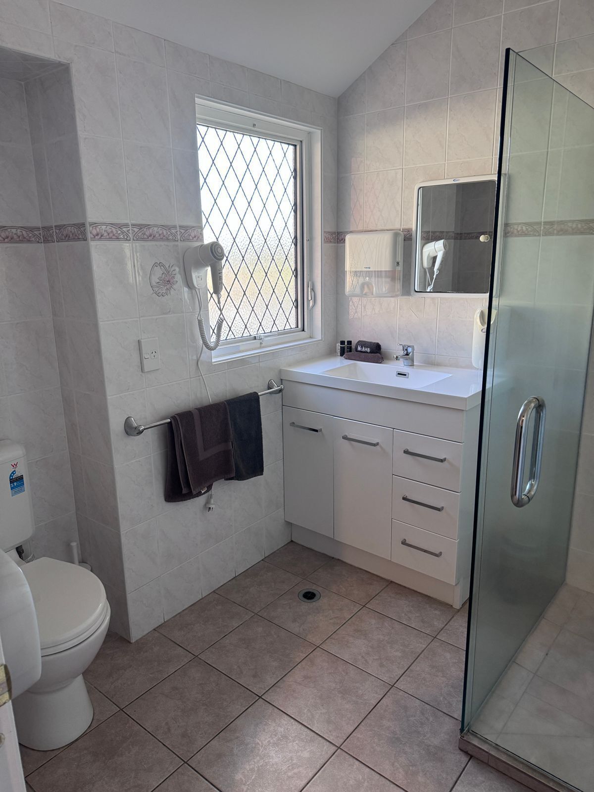 A bathroom with a toilet, a sink with a mirror, a towel rack, and a shower enclosure.