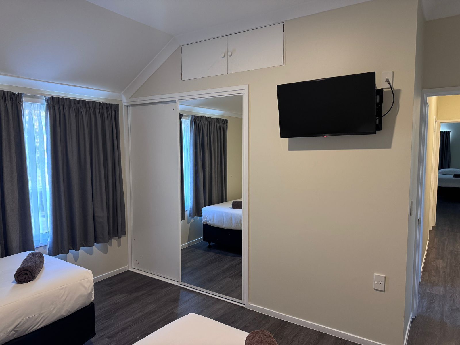 Une chambre d’hôtel avec un lit, un téléviseur fixé au mur et une porte coulissante donnant sur une autre pièce.