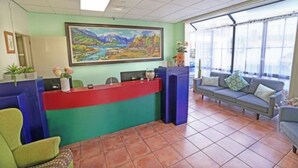 A reception area with a red counter, green and blue seating, and a large landscape painting on the wall. - Anglesea Motel and Conference Centre (Hamilton)