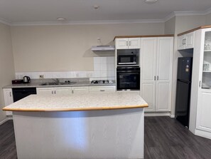 A modern kitchen with white cabinetry, a central island, and built-in appliances including a microwave, oven, and refrigerator. - Anglesea Motel and Conference Centre (Hamilton)