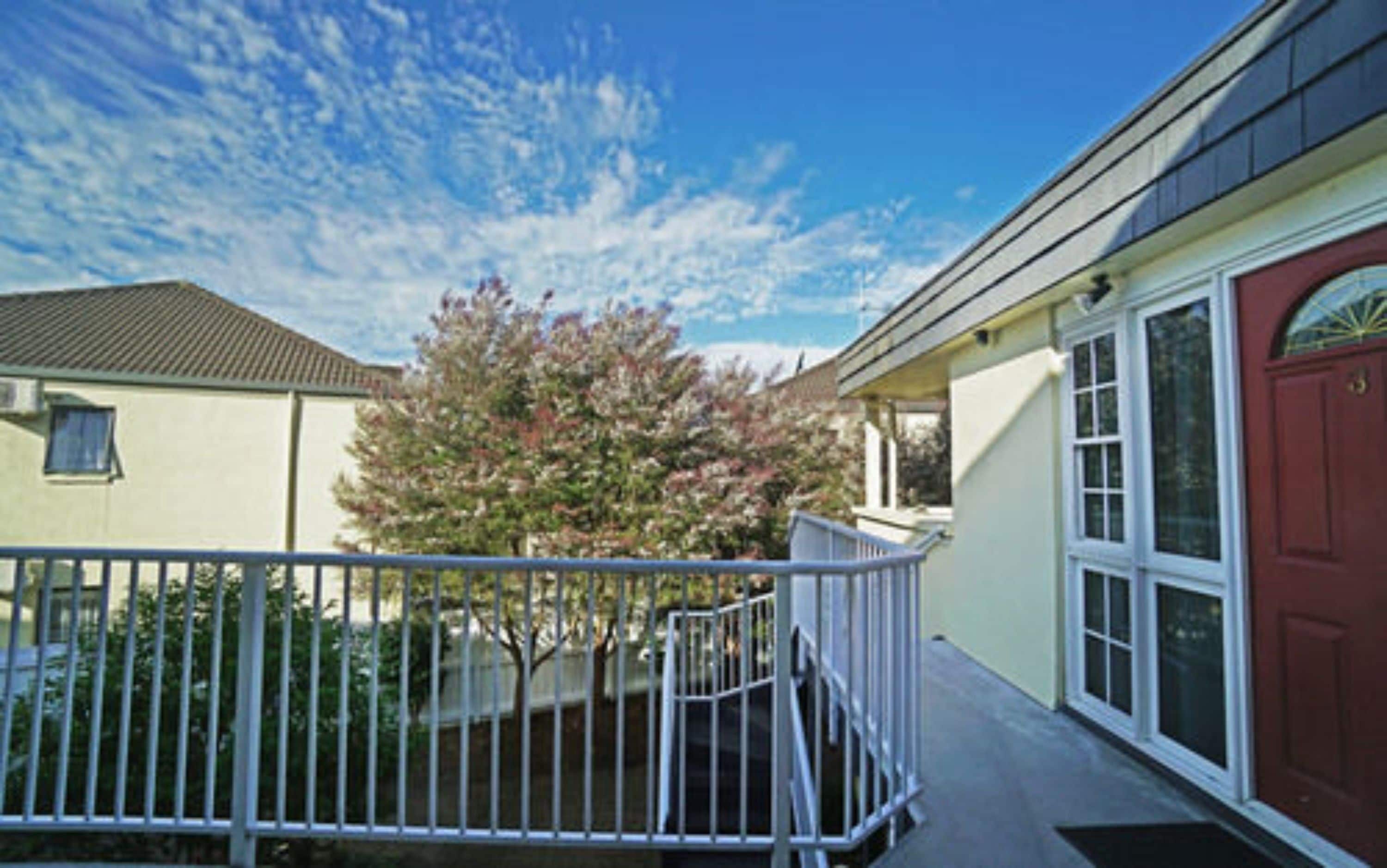A residential building with a red door, a covered porch, and a fenced yard.
