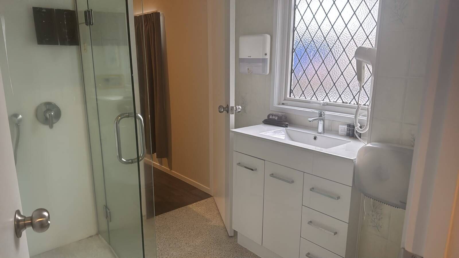 A bathroom with a glass shower enclosure, a white sink with a mirror, and a window with a metal grid.