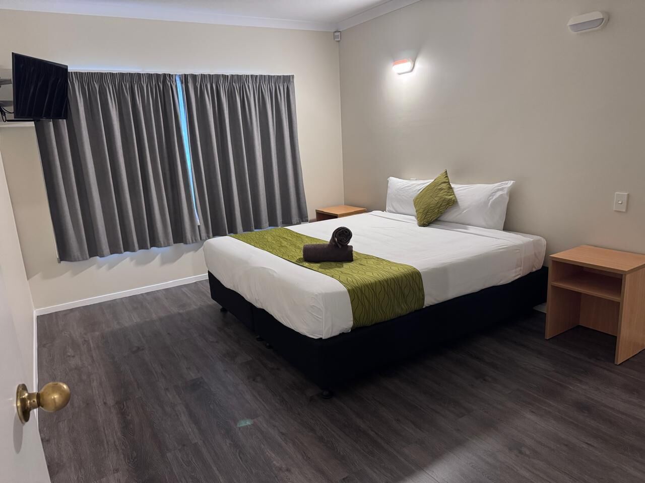 A hotel room with a bed, a nightstand, a TV, and a window with curtains.