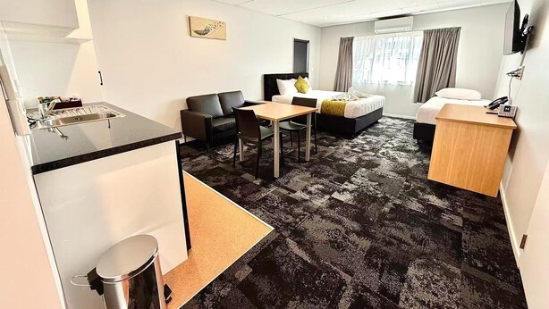 A hotel room with a kitchenette, a dining area, a bed, and a desk. - Anglesea Motel and Conference Centre (Hamilton)