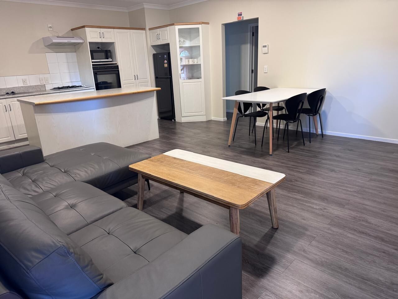 Un salon moderne avec un canapé gris, une table basse en bois et un coin repas comprenant une table blanche et des chaises noires.