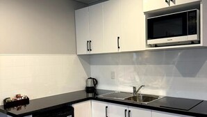 A compact kitchen with white cabinets, a black countertop, a built-in microwave, and a dishwasher. - Anglesea Motel and Conference Centre (Hamilton)