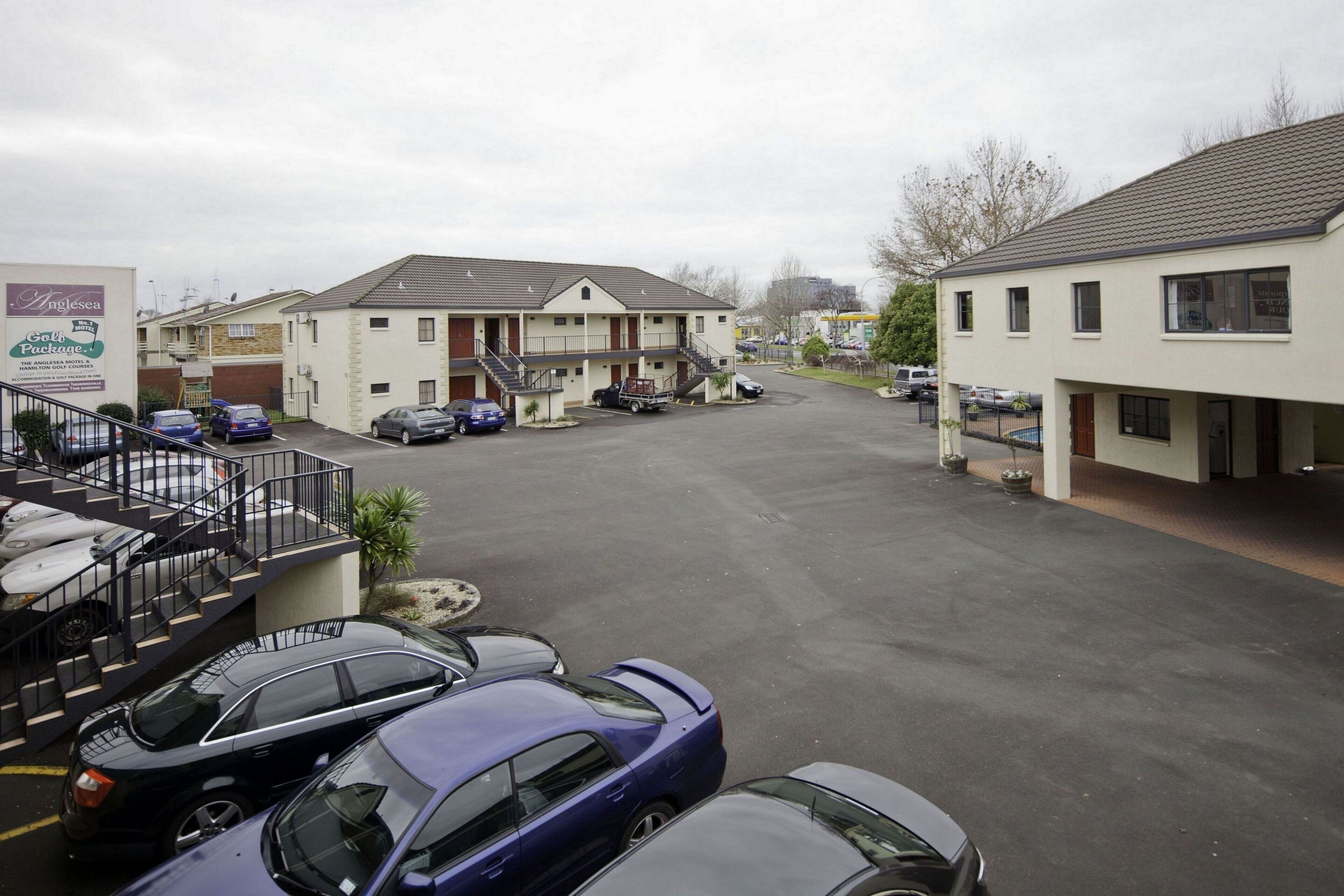 Un parking avec plusieurs voitures, un bâtiment doté d’un escalier et un panneau indiquant « Anglesea ».