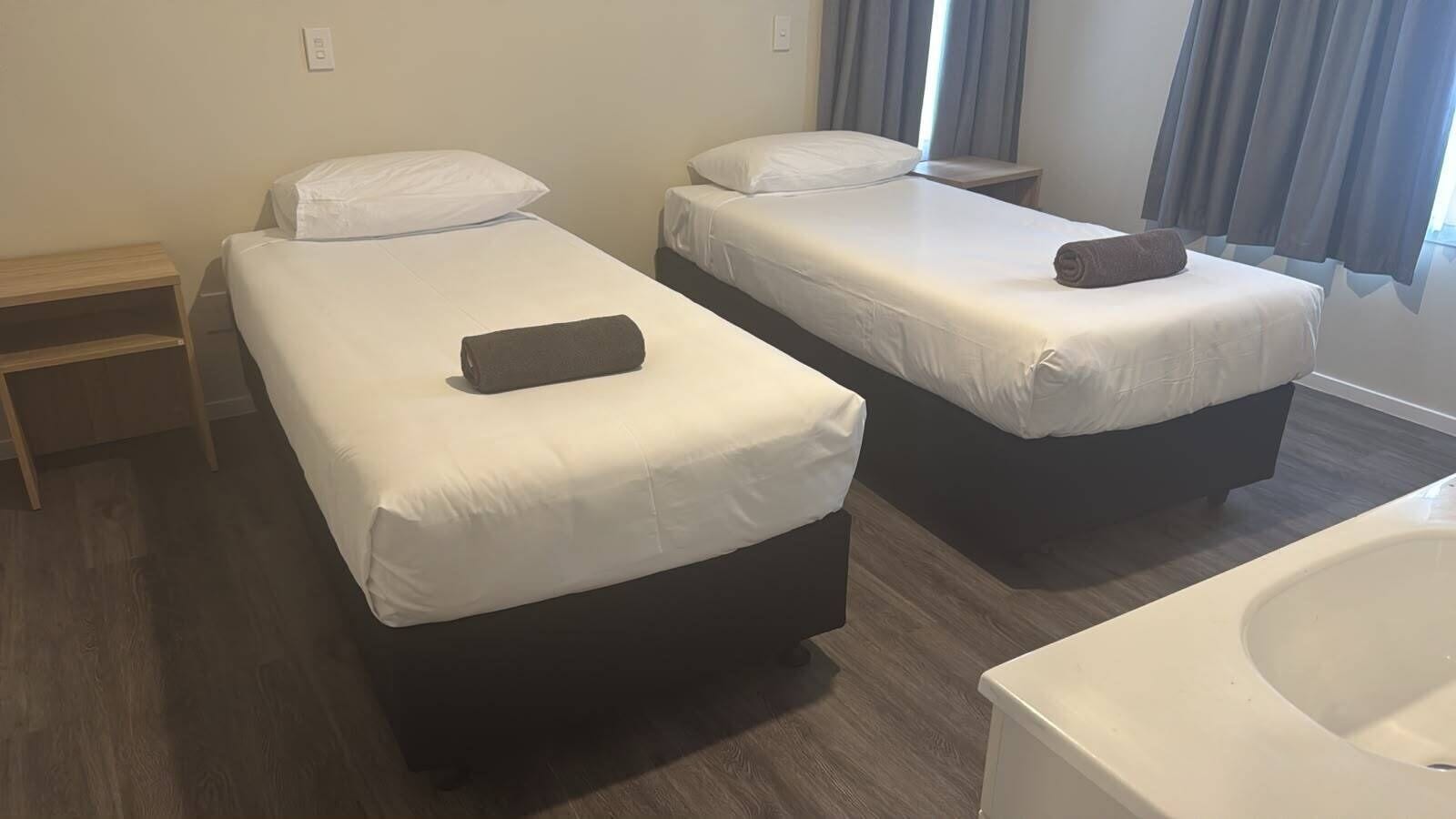 A hotel room with two single beds, a wooden nightstand, a small table, and a bathtub.