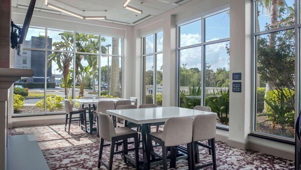 Una habitación amplia con ventanas grandes, alfombra estampada y una mesa con sillas.