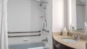 A modern bathroom with a bathtub, a shower with a handheld showerhead, a vanity with a sink, and a mirror.