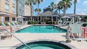 Un área de piscina hotelera con sillones de descanso, sombrillas y un jacuzzi.