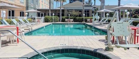 A hotel pool area with lounge chairs, umbrellas, and a hot tub.