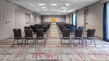 A conference room with rows of chairs, a carpeted floor, and a large window with curtains.