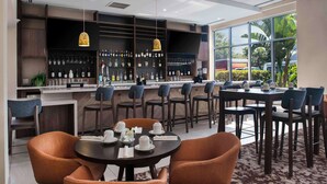 Un área de bar moderna con una variedad de botellas de licor, una barra y distintos arreglos de asientos, incluyendo mesas redondas y sillas.