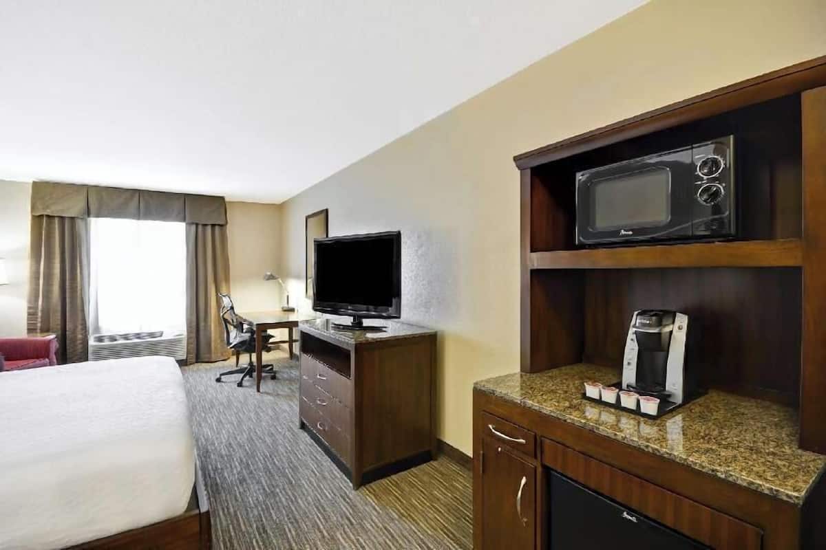 A hotel room with a bed, a desk with a television, a microwave, and a coffee maker.