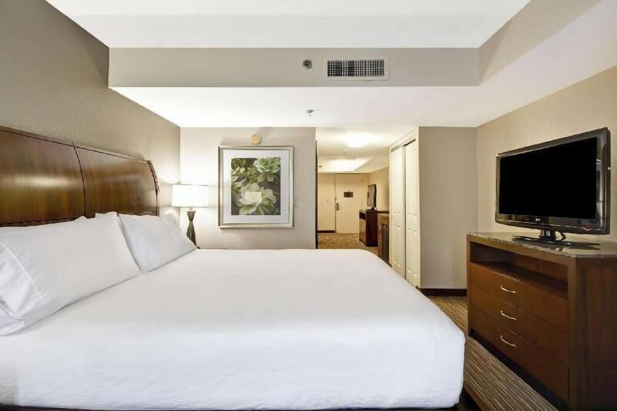 A hotel room with a large bed, a television, a dresser, and a framed picture on the wall.