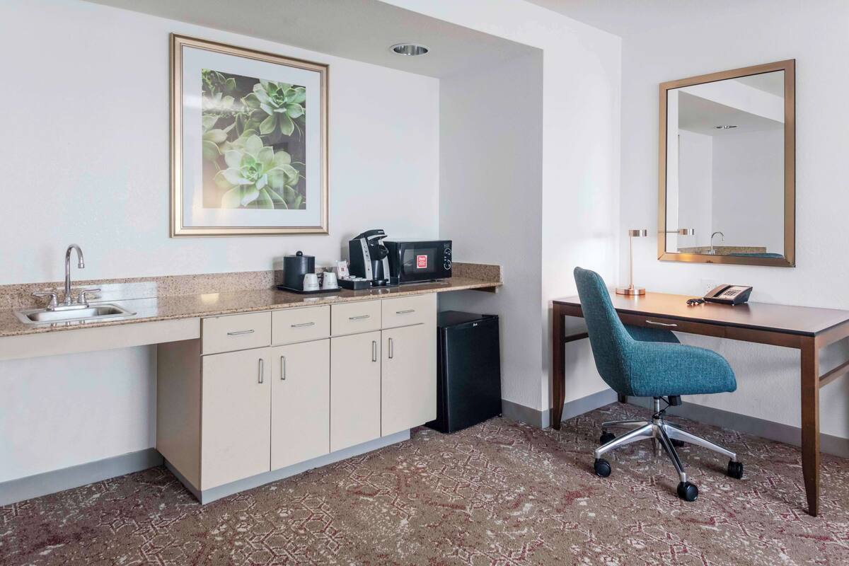Une chambre d’hôtel équipée d’une kitchenette, d’un évier, d’une machine à café, d’un réfrigérateur, d’un bureau avec une chaise et d’un grand miroir.