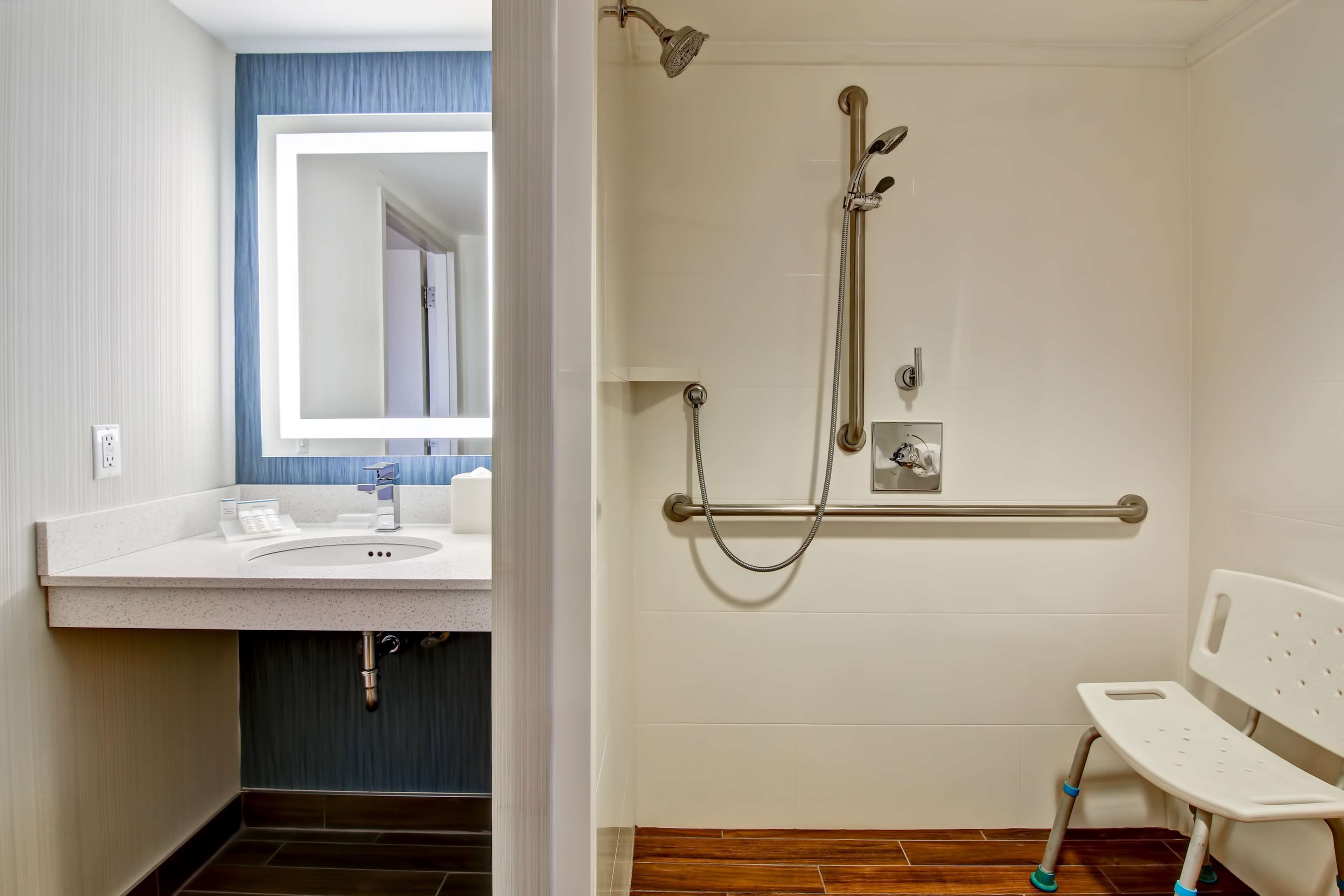 Un baño con lavamanos, espejo, ducha y un banco.