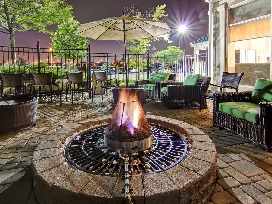 An outdoor patio with a stone fire pit, wicker furniture, and a view of the city at night.