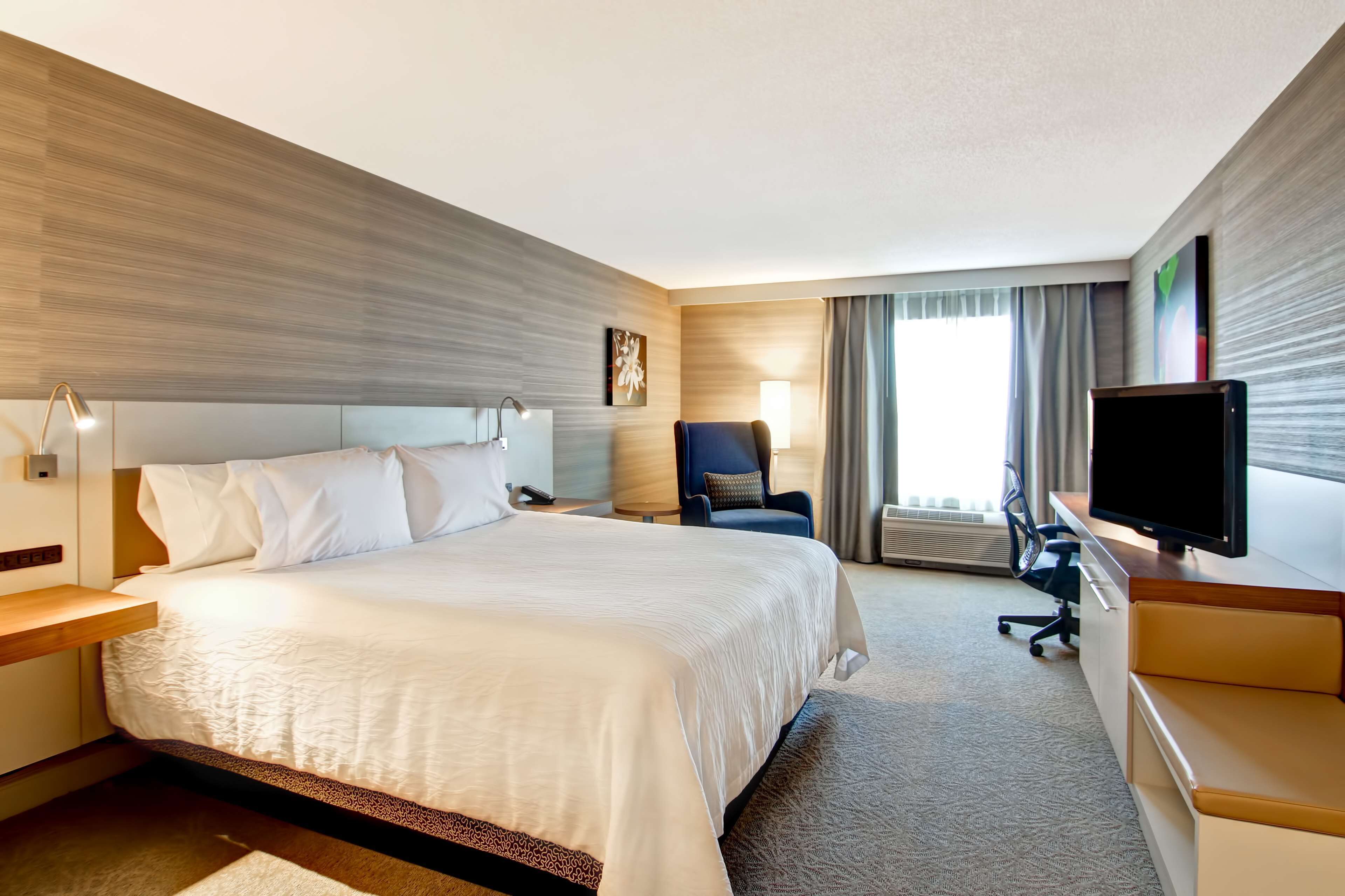 A hotel room with a large bed, a desk, a chair, a TV, and a window with curtains.