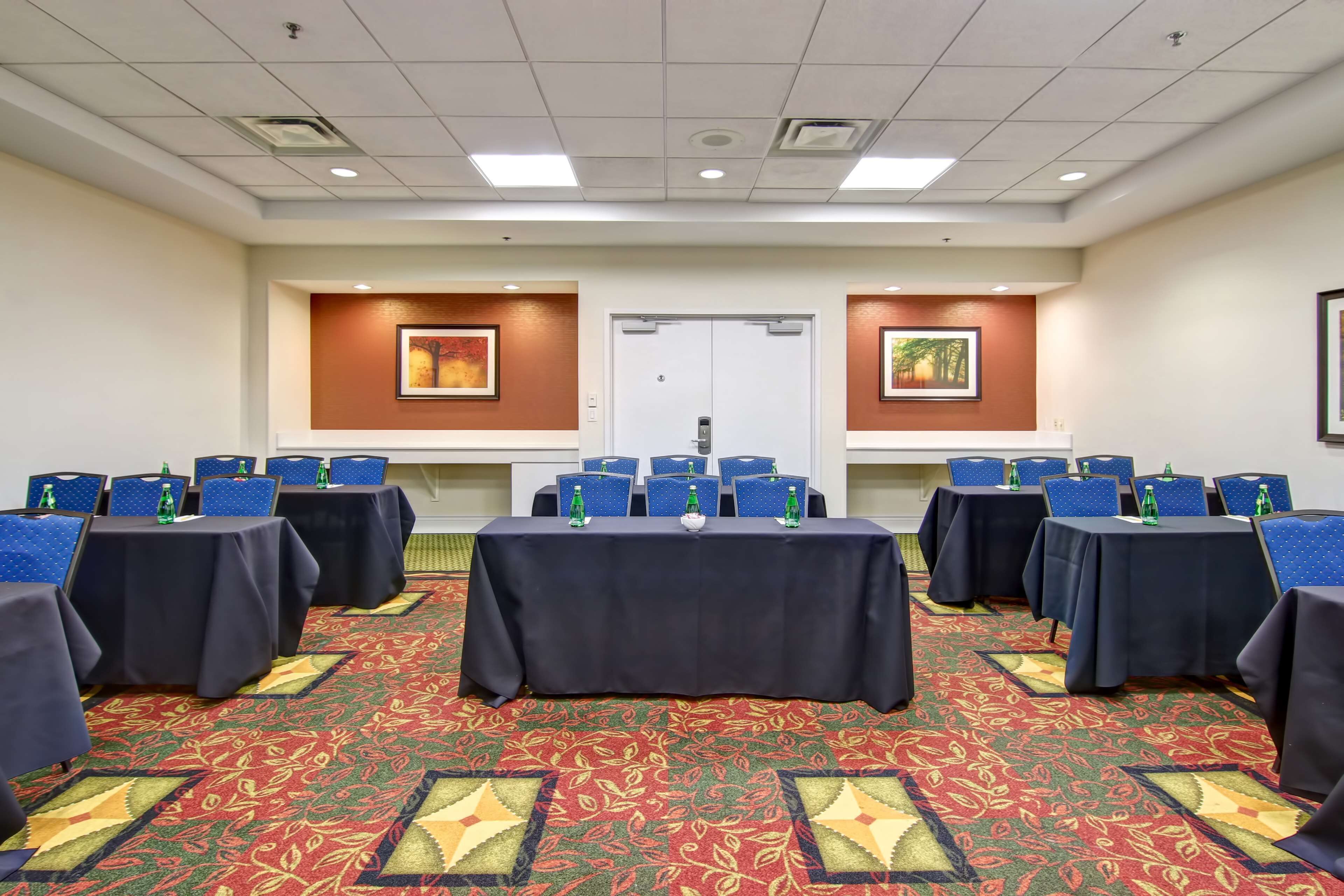 A conference room with multiple tables and chairs, a patterned carpet, and framed artwork on the walls.