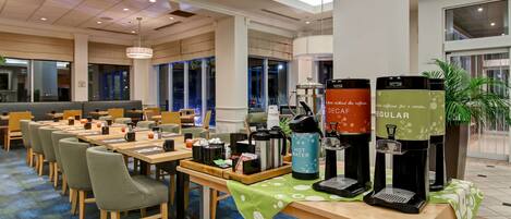 A modern dining area with tables, chairs, and coffee machines.