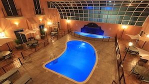Une piscine intérieure dotée d’un toit en verre, entourée de tables et de chaises.