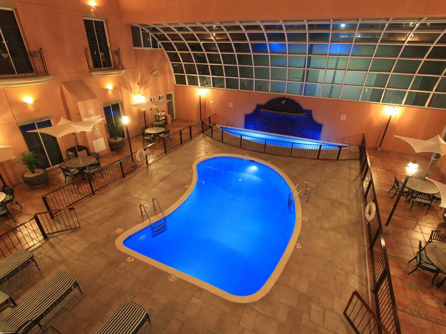Una piscina interior con techo de cristal, rodeada de mesas y sillas.