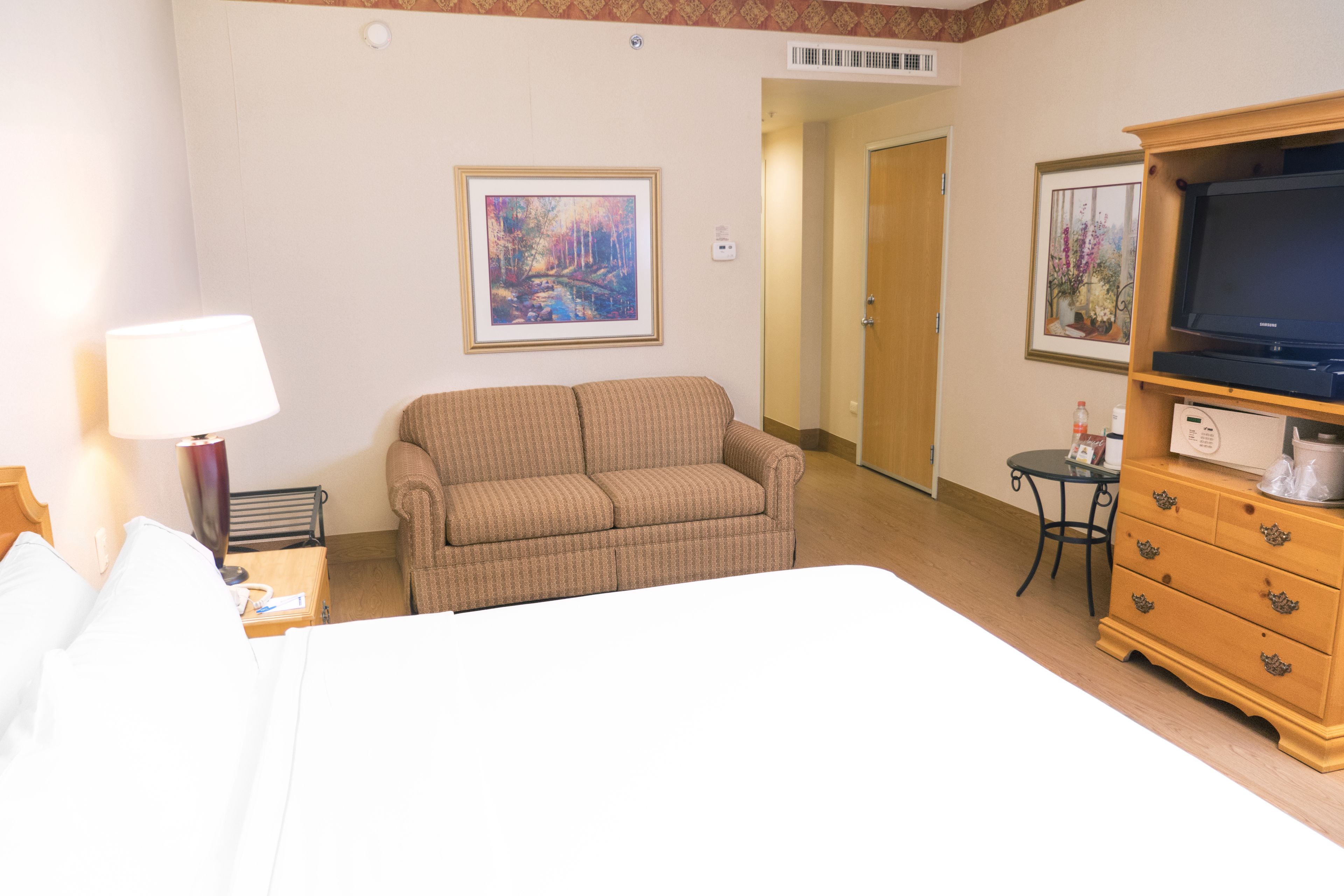A hotel room with a bed, a sofa, a TV, a dresser, and two framed pictures on the wall.