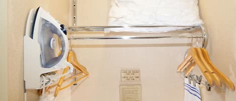 A neatly organized hotel room with a bed, an ironing board, and a check-out time sign.
