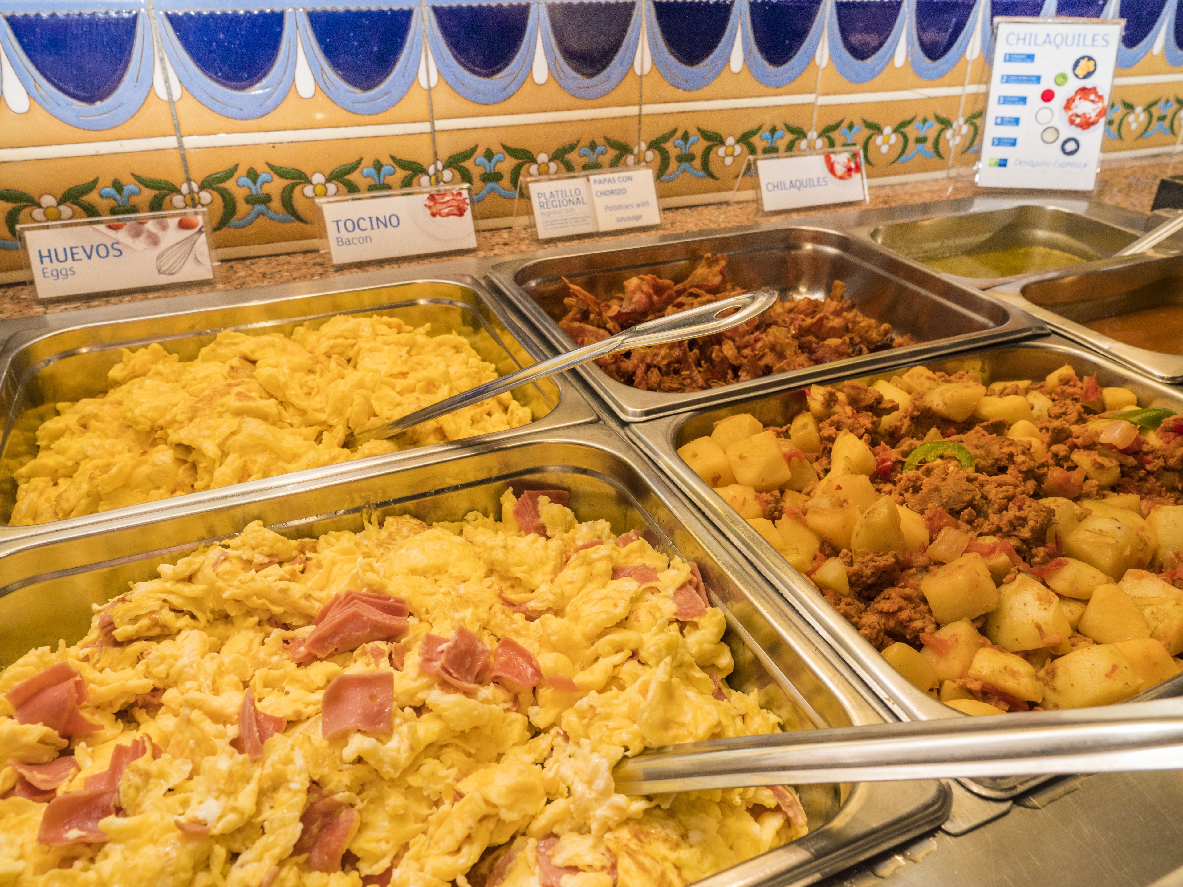 A buffet with labeled food options including eggs, bacon, potatoes, and meat.