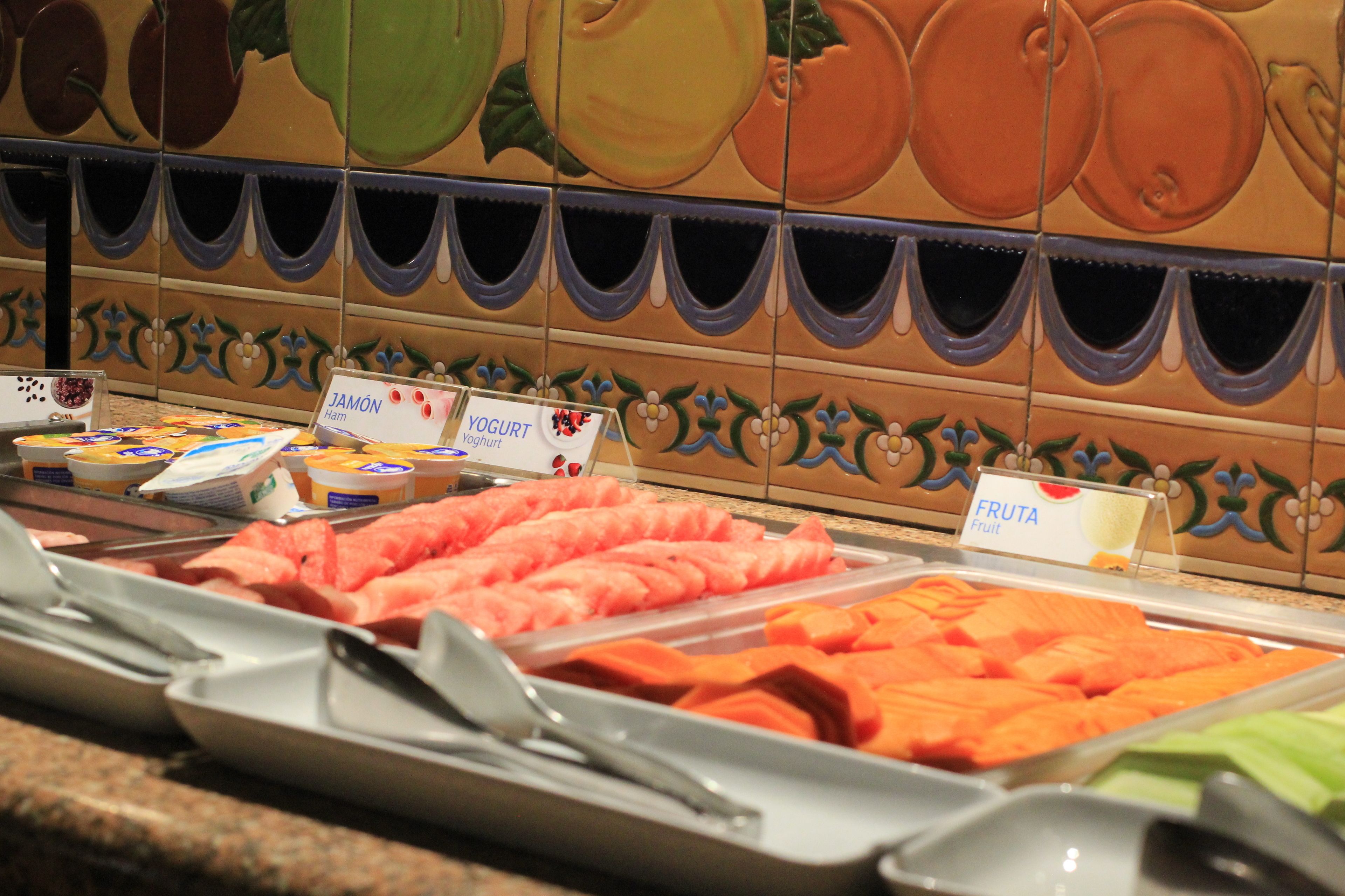 Un buffet proposant une variété de plats, notamment des fruits, des yaourts et du jambon.