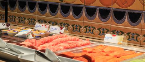 Un buffet proposant une variété de plats, notamment des fruits, des yaourts et du jambon.