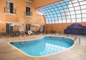Una piscina interior con techo de cristal, rodeada de sillones y mesas.