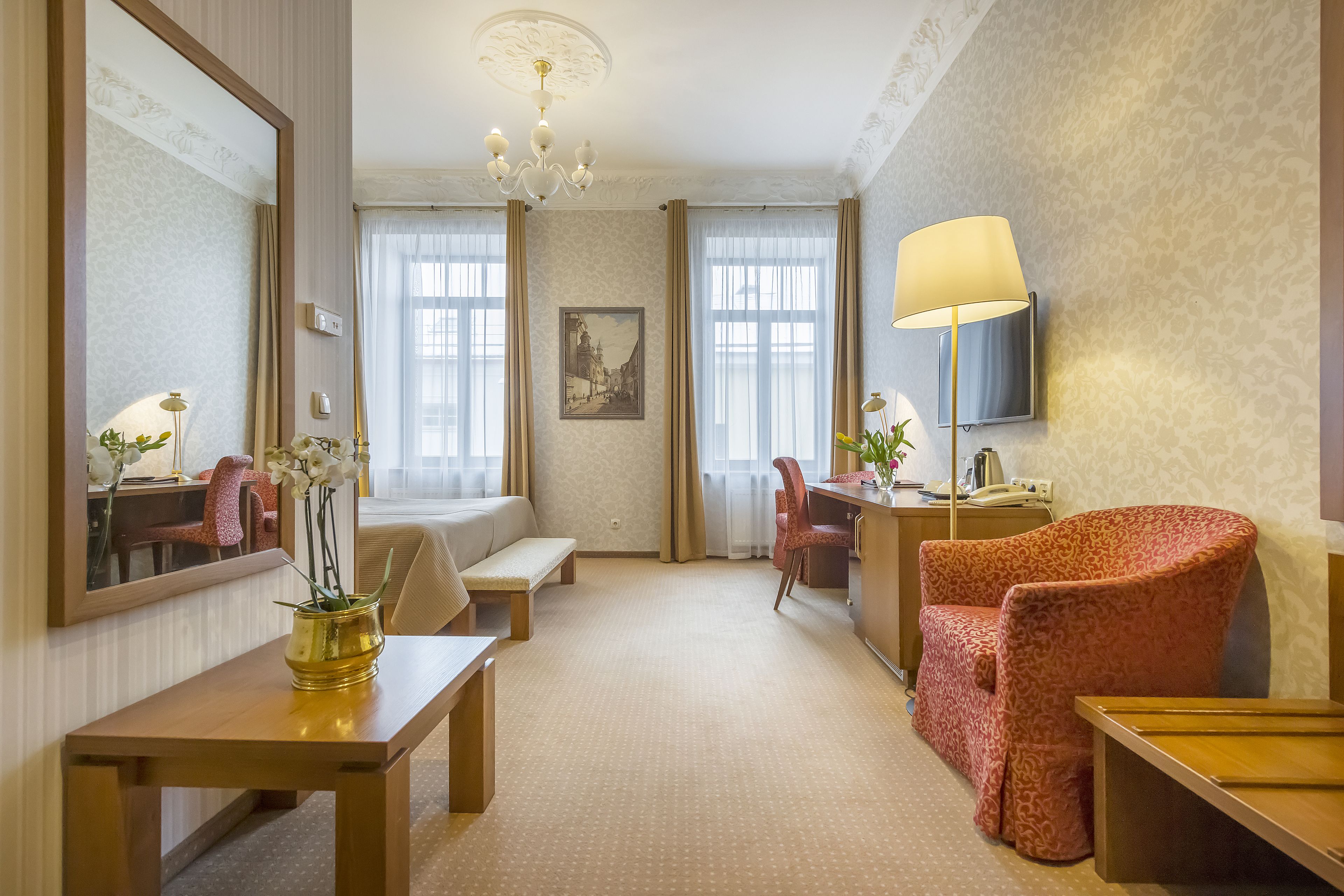 A hotel room with a large bed, a desk with a lamp, a chair, a sofa, and a TV mounted on the wall.