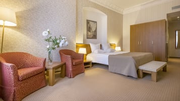 A hotel room with a bed, two armchairs, a small table with a vase of flowers, a lamp, and a wardrobe.
