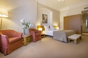 A hotel room with a bed, two armchairs, a small table with a vase of flowers, a lamp, and a wardrobe.