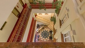 A view of a hotel corridor with a marble staircase, a decorative sunburst wall, and a metal railing.
