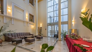 A spacious lobby with a leather sofa, a reception desk, and a red table with a floral arrangement.