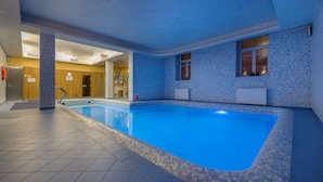 An indoor swimming pool with tiled flooring and walls, a clear pool edge, and a visible door leading to another room.