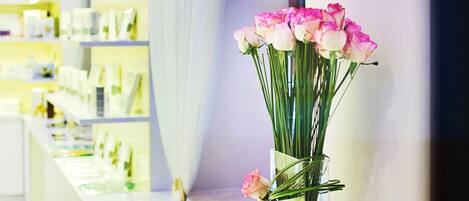 A modern interior with a reception desk, a vase of pink flowers, and shelves with products.