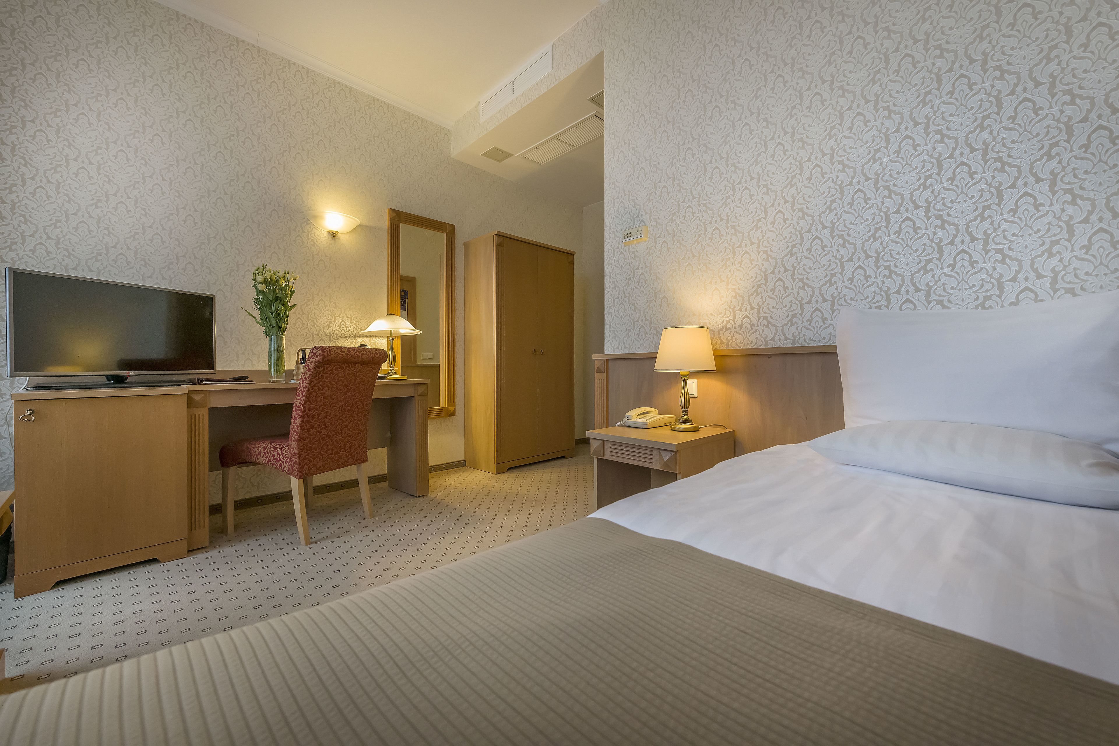 A hotel room with a bed, desk, chair, TV, lamps, and a telephone.