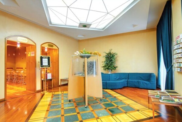 A hotel lobby with a geometric ceiling design, a blue sofa, a small table with books, and a patterned carpet. - Hotel Corot (Rome)